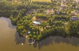 Luftaufnahme eines Ferien- und Theatervillages am See mit Bäumen und Gebäuden.