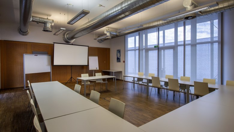Seminarraum mit Tischen, Stühlen und Projektionsleinwand.