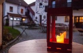 Laterne mit brennender Kerze auf einem Holztisch im Innenhof eines Landhotels.