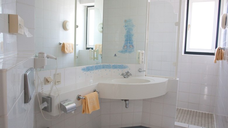 Helles Badezimmer mit Waschbecken, Spiegel, Dusche und Handt&uuml;chern.