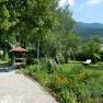 Ein gepflegter Garten mit Kiesweg, Blumenbeeten, einem Pavillon und Liegest&uuml;hlen vor einer Bergkulisse.