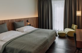 Modern eingerichtetes Hotelzimmer mit Doppelbett, grünem Sessel und Schreibtisch.