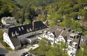 Luftaufnahme eines großen Gebäudekomplexes umgeben von grünen Bäumen und Hügeln.