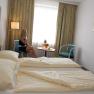 Hotelzimmer mit Doppelbett, Frau telefoniert am Tisch mit Obst.
