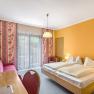 Hotelzimmer mit Doppelbett, gelben W&auml;nden, rotem Sofa und Balkon.