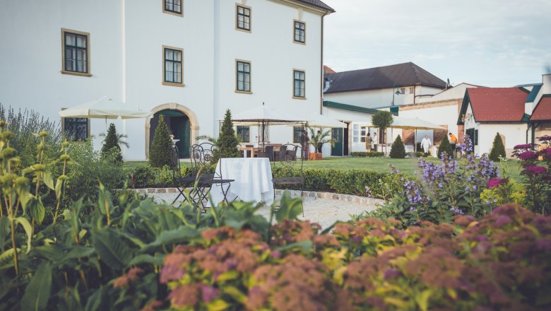 Gartenansicht von Schloss Raggendorf mit Blumen, Tischen und Stühlen im Vordergrund.