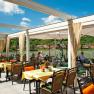 Restaurantterrasse mit Blick auf einen Fluss und gr&uuml;ne H&uuml;gel im Hintergrund.