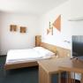 Modern eingerichtetes Hotelzimmer mit Bett, Schreibtisch, Fernseher und Wanddekoration.