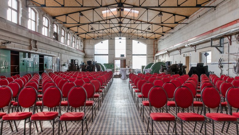 Innenansicht einer alten Turbinenhalle mit roten Stühlen und industriellen Maschinen.