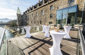 Terrasse mit Stehtischen vor einem historischen Gebäude mit Glasfassade.