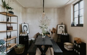 Ein stilvoll eingerichteter Raum mit Holztisch, Regalen, Pflanzen und Kunstwerken an den W&auml;nden.