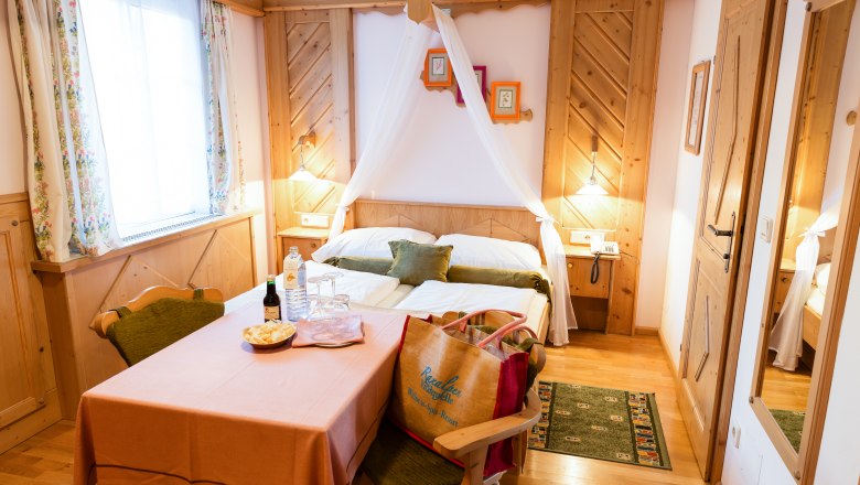 Gemütliches Doppelzimmer mit Holzmöbeln, einem Tisch mit Getränken und Snacks, und einem Bett mit Baldachin.