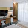 Modernes Hotelzimmer mit Schreibtisch, Fernseher und Vorh&auml;ngen.