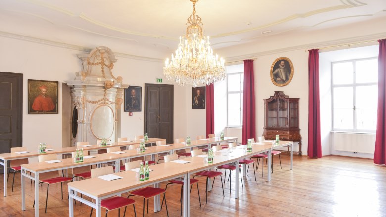 Eleganter Seminarraum mit Kronleuchter, Holzboden und Porträts an den Wänden.