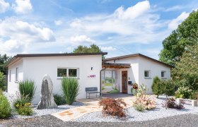 Modernes, weißes Gebäude mit Garten und Kiesweg, blauer Himmel im Hintergrund.