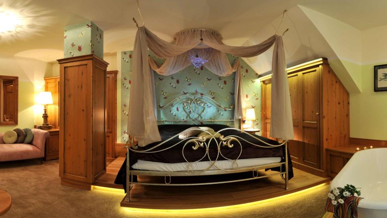 Ein luxuri&ouml;ses Schlafzimmer mit Himmelbett, Holzm&ouml;beln und Badewanne.