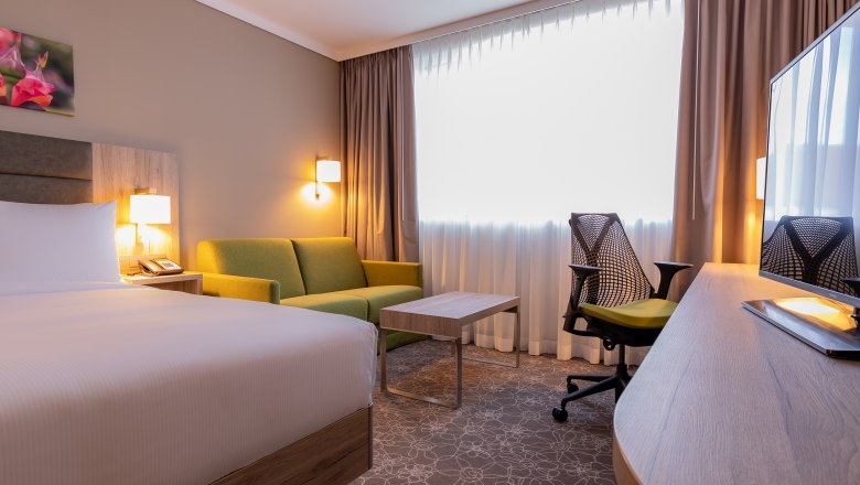 Hotelzimmer mit Bett, grünem Sofa, Schreibtisch und Stuhl.