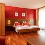 Gem&uuml;tliches Hotelzimmer mit Doppelbett, Holzm&ouml;beln und roten Akzenten.