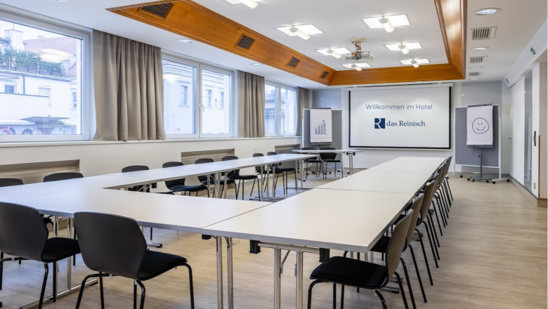 Seminarraum im Das Reinisch Hotel mit Tischen, Stühlen und Präsentationsleinwand.