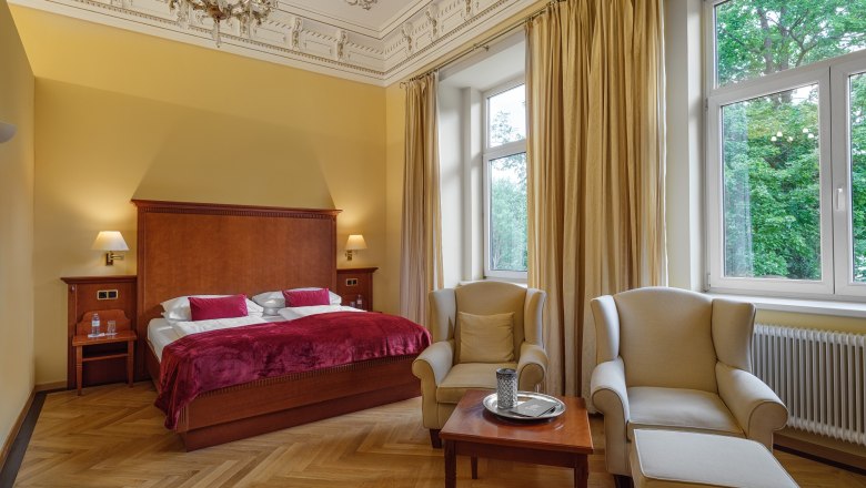 Elegantes Hotelzimmer mit Doppelbett, Sesseln und großen Fenstern.