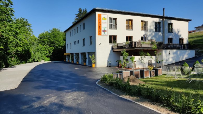 Gebäude mit der Aufschrift 'Brandtner', umgeben von Bäumen und einem Parkplatz.