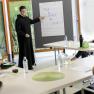 Ein Seminar im Stift Seitenstetten mit einem Vortragenden in M&ouml;nchskleidung, der auf ein Flipchart zeigt. Teilnehmer sitzen an Tischen.