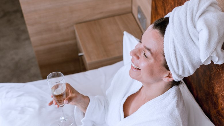 Zwei Personen im Bademantel fr&uuml;hst&uuml;cken im Bett mit Sekt und Dessert.