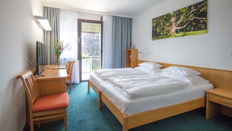 Hotelzimmer mit Doppelbett, Schreibtisch, Stuhl und Balkon.