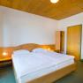 Ein einfach eingerichtetes Hotelzimmer mit Doppelbett, Holzdecke, Schrank und Nachttischlampen.