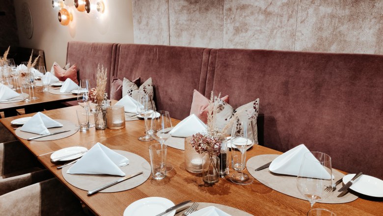 Ein elegant gedeckter Tisch in einem Restaurant mit wei&szlig;en Servietten, Gl&auml;sern und Besteck auf Holzoberfl&auml;che.