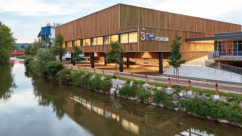 Modernes Gebäude der Messe Wieselburg mit Holzfassade und Fluss im Vordergrund.