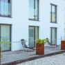 Moderne Terrasse mit Liegest&uuml;hlen und Pflanzen vor einem Geb&auml;ude mit gro&szlig;en Fenstern.