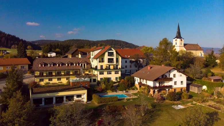 Luftaufnahme eines Dorfes mit einem Hotel, einem Pool und einer Kirche im Hintergrund.
