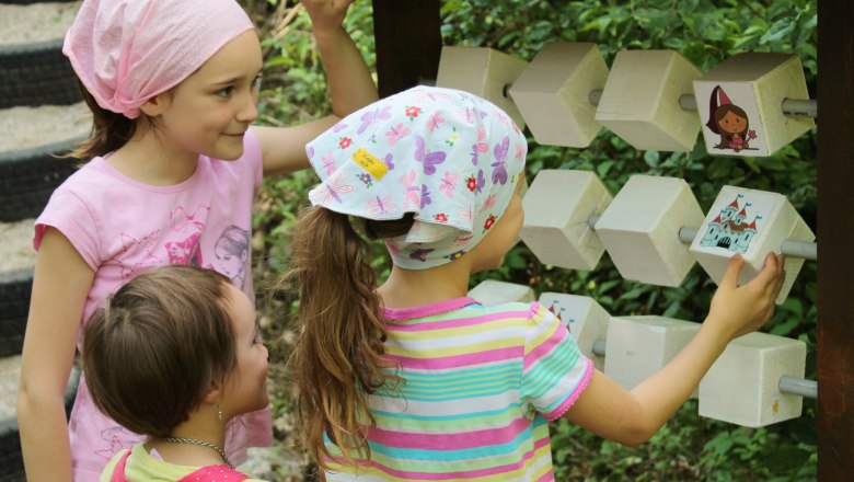 Drei Kinder spielen an einem h&ouml;lzernen Spielger&auml;t im Freien.