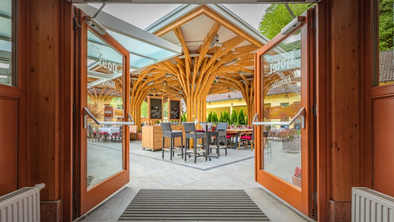 Offene Glast&uuml;ren f&uuml;hren zu einer Terrasse mit Holzdach und Sitzgelegenheiten.