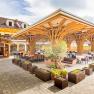Terrasse mit Holzdach und Tischen, umgeben von Pflanzen.