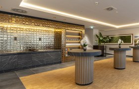 Moderner Raum für Seminar Kaffeepausen mit goldener Wand, schwarzen Marmortischen und Orchideen.