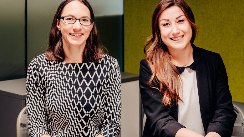 Zwei Frauen sitzen nebeneinander und l&auml;cheln in die Kamera.