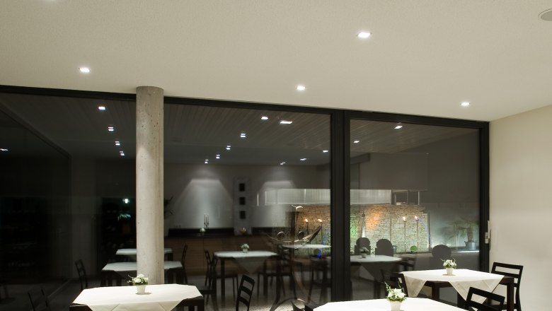 Moderner Fr&uuml;hst&uuml;cksraum mit Tischen und St&uuml;hlen, dekoriert mit wei&szlig;en Tischdecken und Blumen.