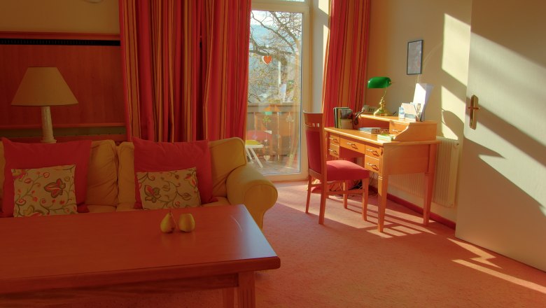 Ein gemütliches Zimmer mit Sofa, Schreibtisch und großem Fenster mit Vorhängen.