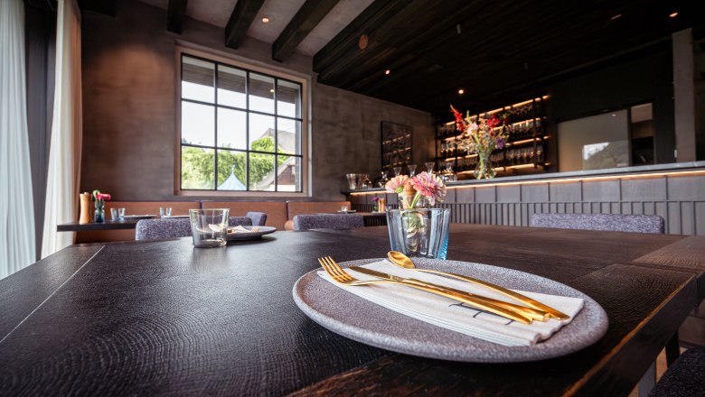 Elegantes Restaurant mit gedecktem Tisch, goldfarbenem Besteck und Blumen.