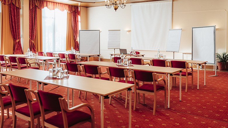 Ein Seminarraum mit roten St&uuml;hlen, Tischen, Flipcharts und einem Projektor.