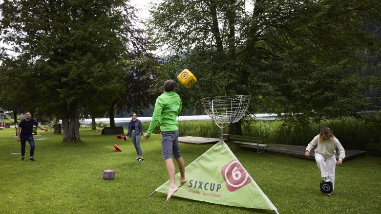 Menschen spielen ein Outdoor-Wurfspiel mit gro&szlig;en W&uuml;rfeln auf einer Wiese.