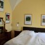 Schlafzimmer mit Doppelbett, gelben W&auml;nden und mehreren gerahmten Bildern an der Wand.