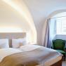 Gem&uuml;tliches Schlafzimmer mit Doppelbett, gr&uuml;nem Sessel und gew&ouml;lbter Decke.