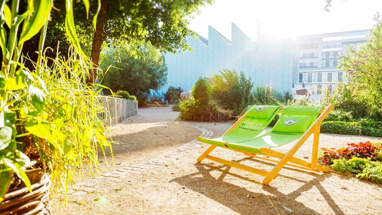 Gartenbereich des Museums Niederösterreich mit grünen Liegestühlen und Pflanzen im Sonnenlicht.