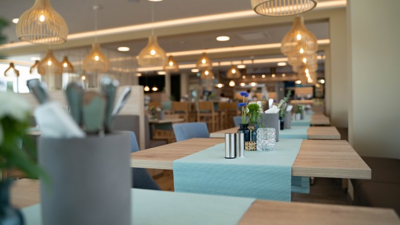 Innenansicht eines modernen Cafés mit Holztischen, blauen Tischläufern und hängenden Lampen.