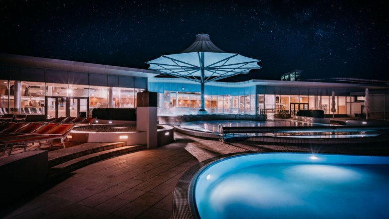 Nachtaufnahme eines modernen Spa-Bereichs mit beleuchteten Pools und einem gro&szlig;en Sonnenschirm.