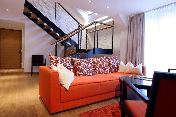 Moderne Suite mit oranger Couch, dekorativen Kissen und Treppe im Hintergrund.
