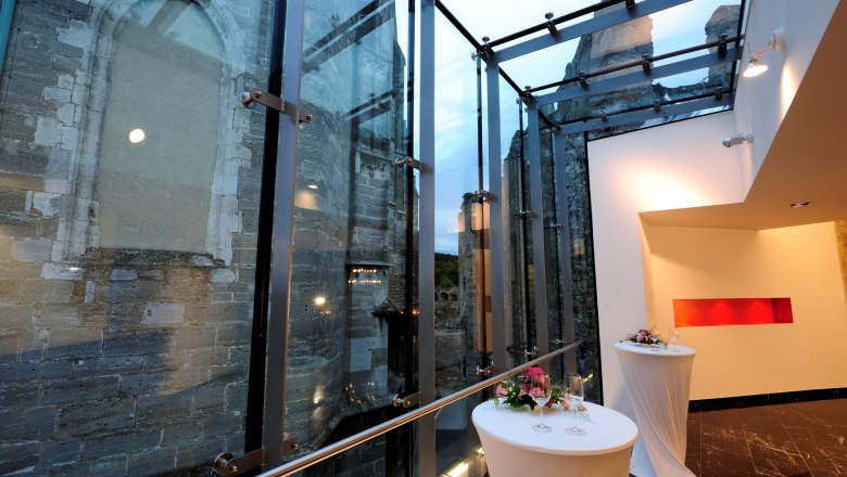 Moderne Glasarchitektur neben alter Steinmauer mit dekorierten Stehtischen.